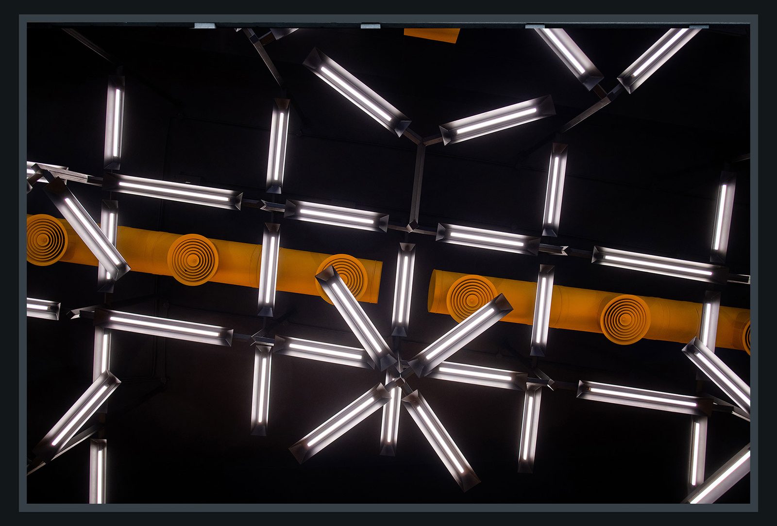 Cheese on Top ceiling: crossed tubular light fixtures radiating from a central yellow hub against a black ceiling